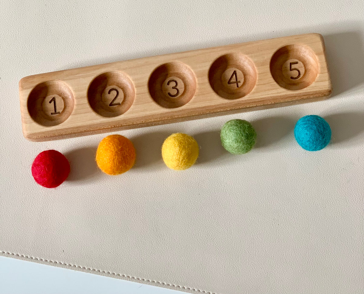 Wooden counting tray numbered 1 to 5 with five colorful felt balls in red, orange, yellow, green, and blue below it