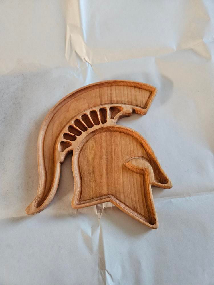 Carved wooden tray shaped like a Spartan helmet with detailed crest and cutout sections on a light surface