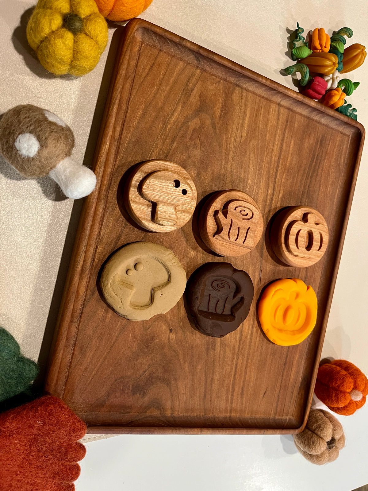 Wooden autumn-themed playdough stamps and matching dough impressions on a wooden tray surrounded by felt pumpkins and gourds
