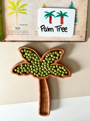 Wooden palm tree-shaped tray filled with green peas next to a card illustrating palm trees and labeled "Palm Tree
