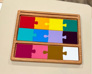 Colorful rectangular wooden puzzle pieces in a light wood tray arranged in three rows on a light background