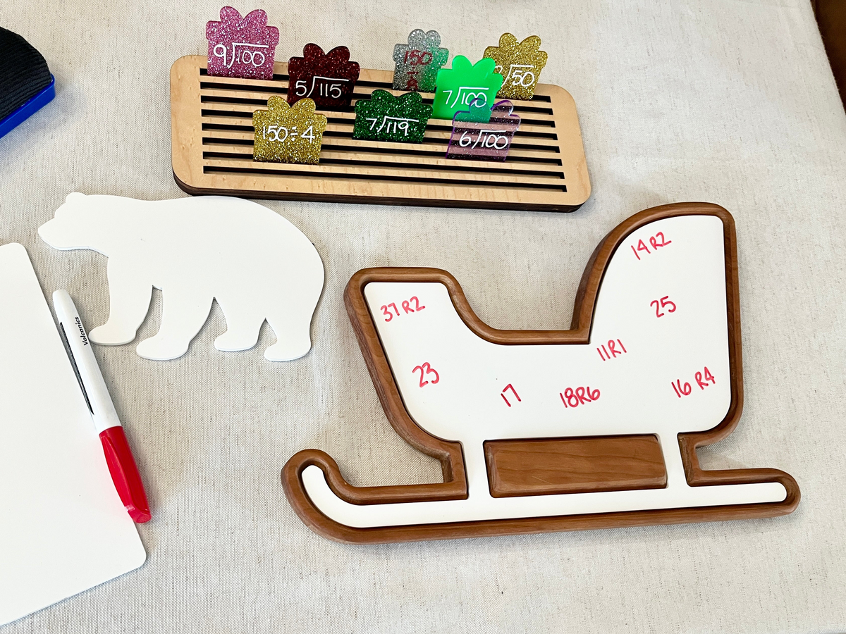 Wooden sled-shaped sensory tray with red marker, whiteboard, wooden polar bear cutout, and colored number clips on beige surface