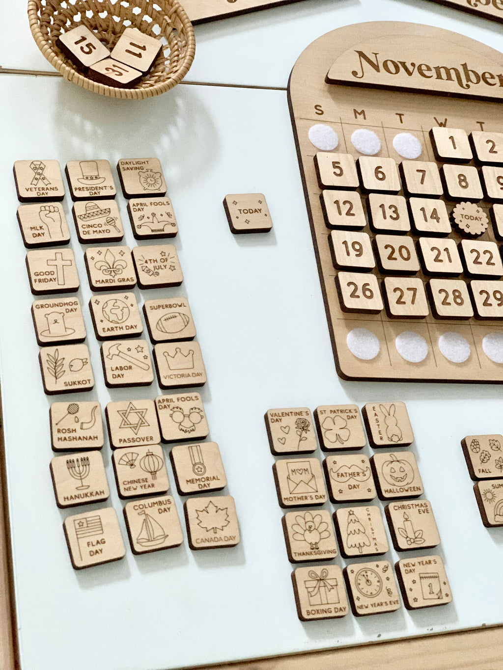 Wooden perpetual calendar with month name, date tiles, and various engraved holiday and event marker tiles on white surface