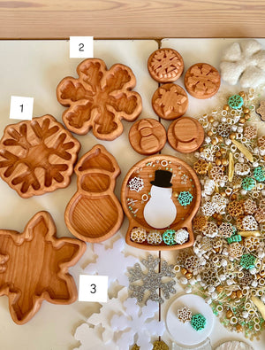Assortment of carved wooden trays shaped like snowflakes, snowman, and round discs with winter-themed decorations on a table
