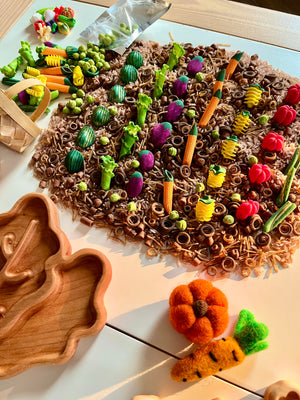 Assorted colorful felt vegetables and pastas arranged neatly on textured brown rice with wooden trays nearby