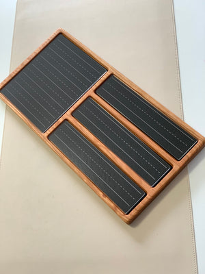 Wooden tray with four black panels featuring dashed lines for writing practice on a light beige surface