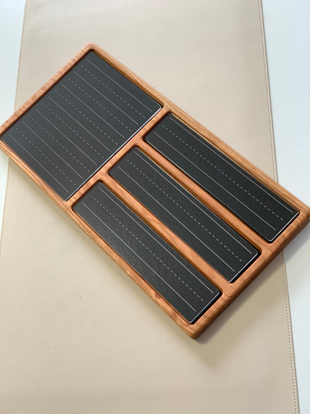 Wooden tray with four black panels featuring dashed lines for writing practice on a light beige surface