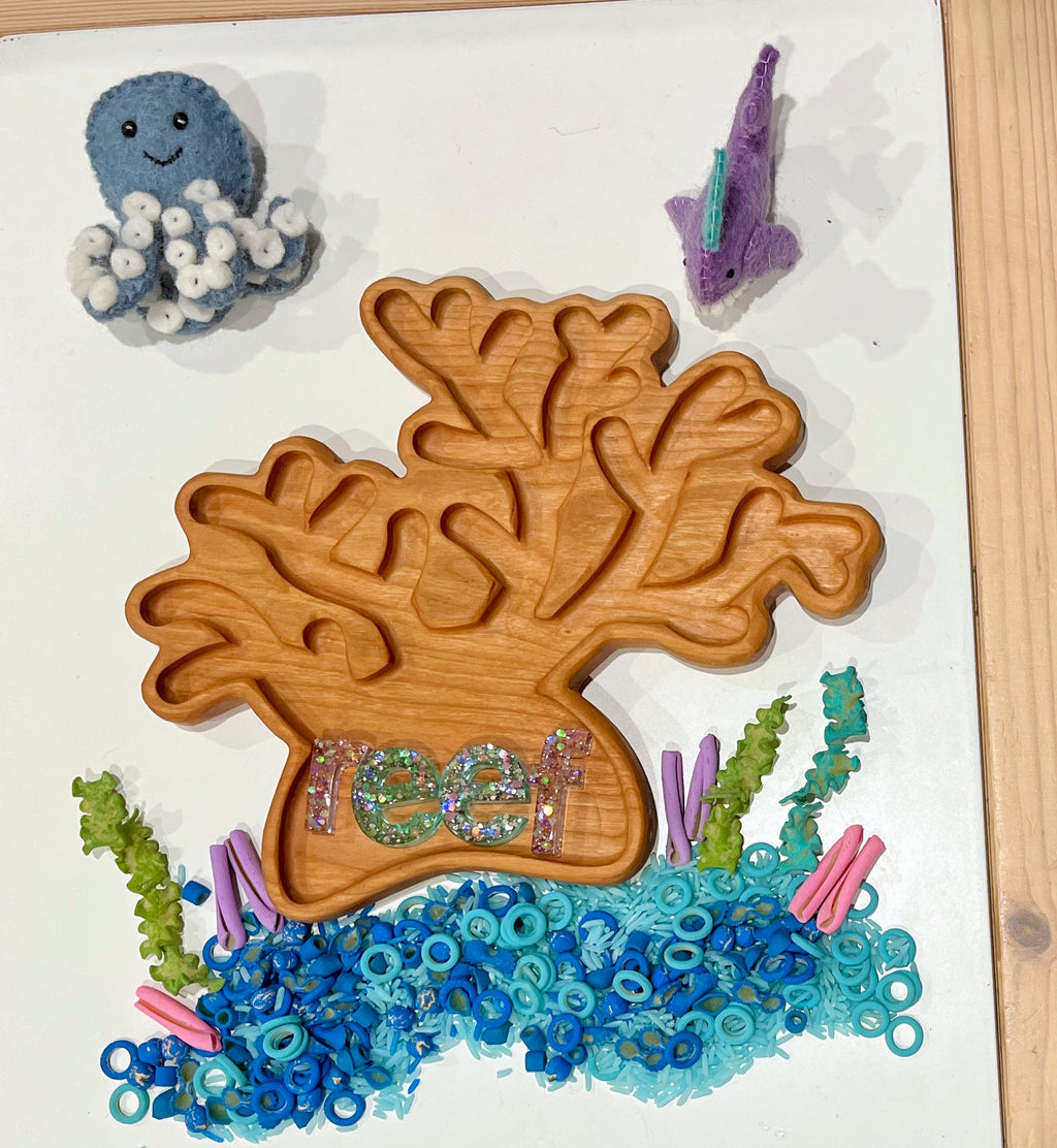 Wooden coral-shaped tray filled with blue and green sea-themed beads and surrounded by felt sea creatures on white surface