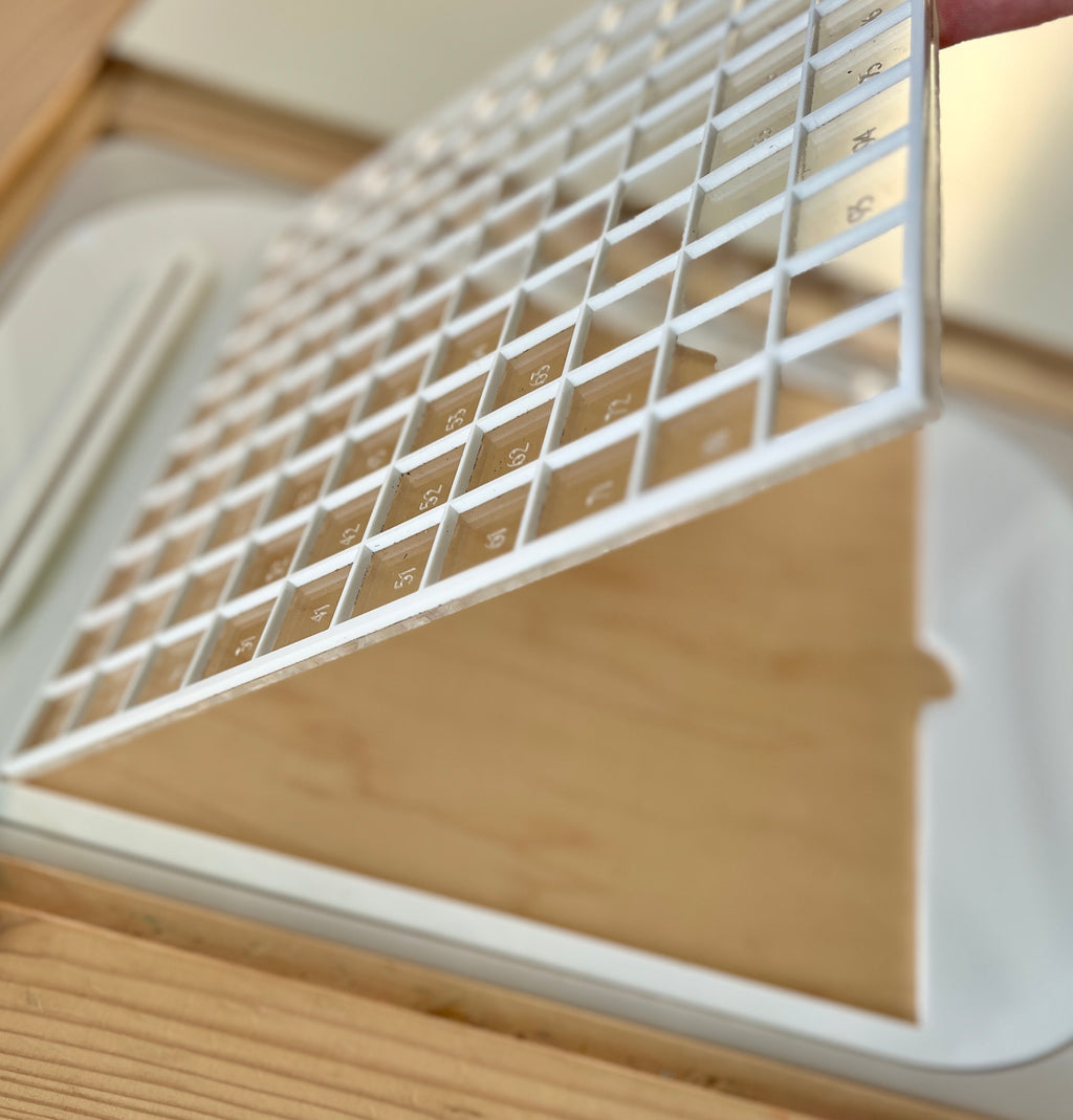 White plastic grid tray with numbered compartments positioned above a light wooden box on a wooden surface