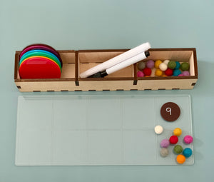 Wooden organizer holding colorful translucent discs, white markers, and multicolored felt balls on a light blue surface