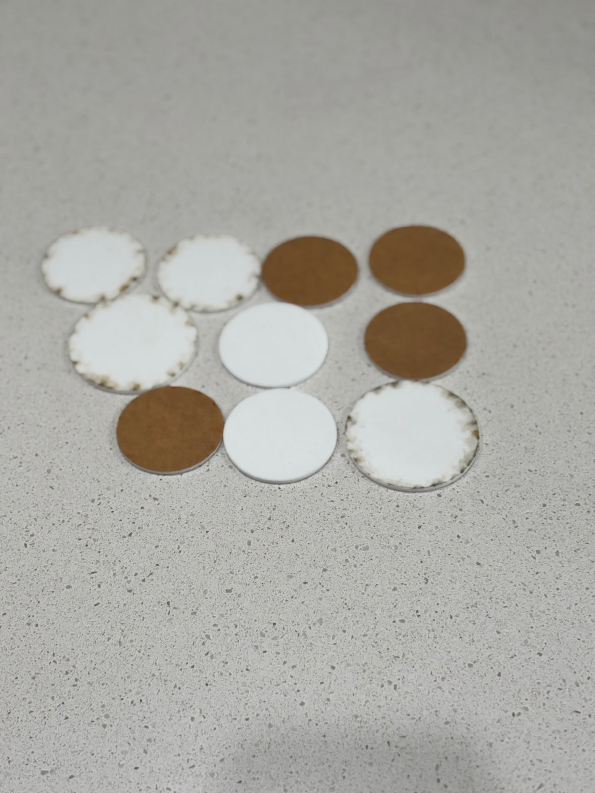 Assorted round coasters in white felt and brown wood arranged on a light speckled surface