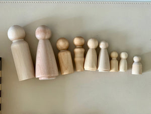Line of smooth unfinished wooden peg doll figures in varying sizes on a neutral surface