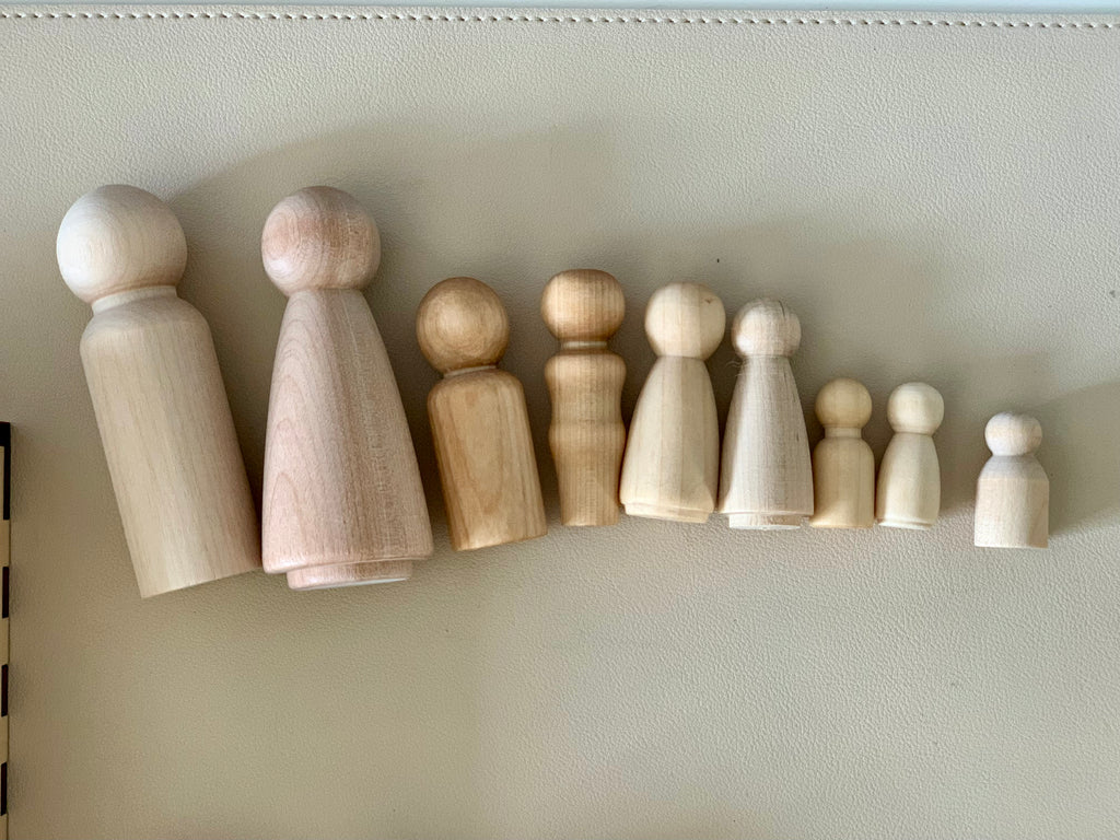Line of smooth unfinished wooden peg doll figures in varying sizes on a neutral surface