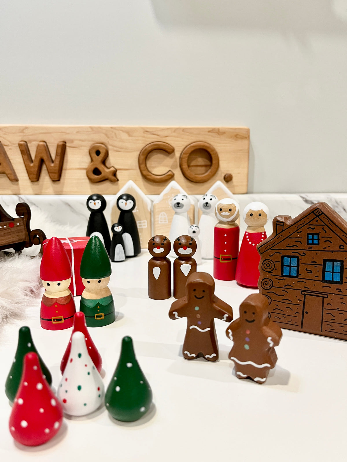 Wooden holiday figurines including gingerbread people, elves, penguins, polar bears, and a brown house on white surface