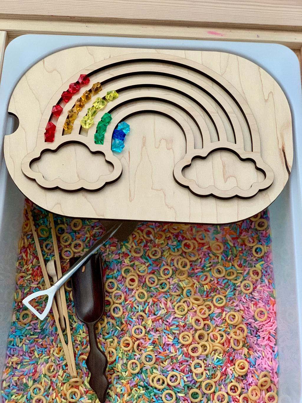 Wooden rainbow puzzle with colorful translucent beads on a sensory bin filled with dyed rice and cereal rings