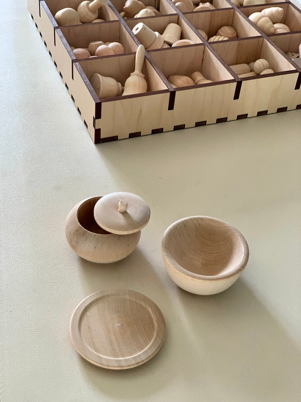 Unfinished natural wood small pot with lid and bowl alongside wooden game pieces in a divided storage box
