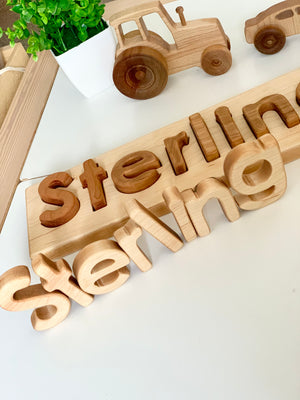 Personalized hardwood name puzzle with natural and dark wood letters spelling Sterling on white surface with wooden toy vehicles