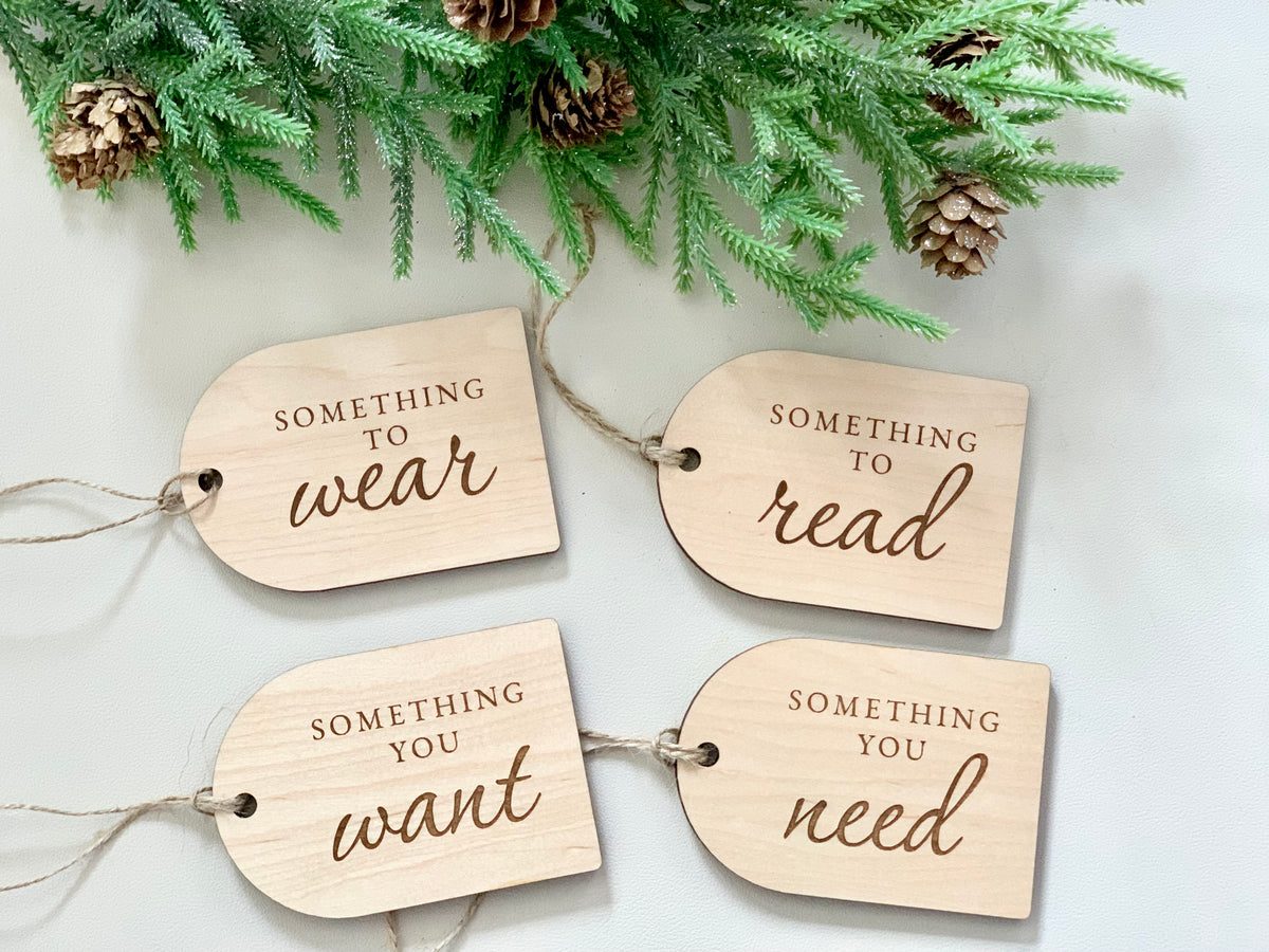 Set of four maple plywood Christmas gift tags engraved with "Something you want," "need," "read," and "wear" with pine decoration