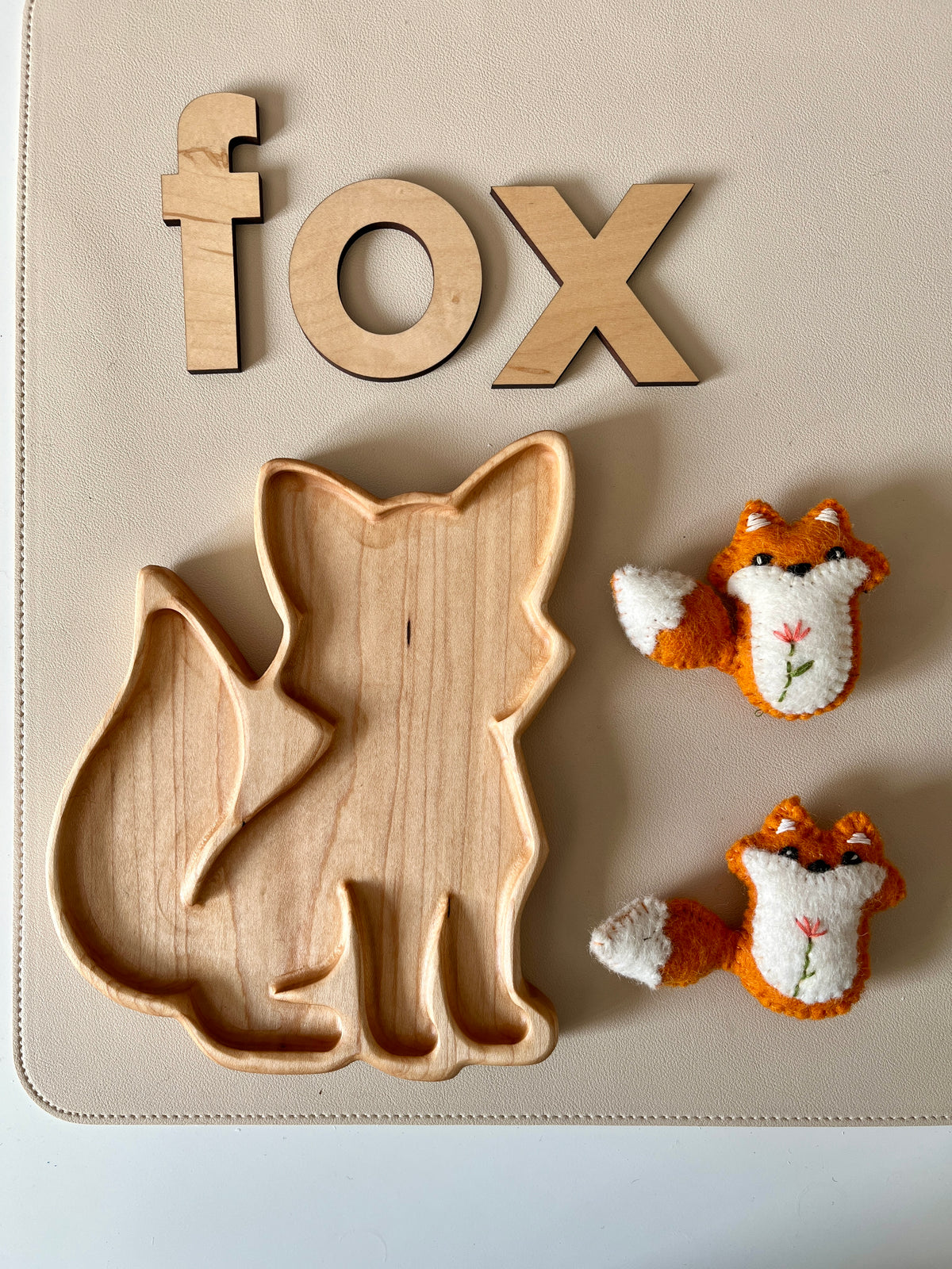 Wooden tray carved in the shape of a fox with wooden letters spelling "fox" and two small knitted fox toys on a beige surface