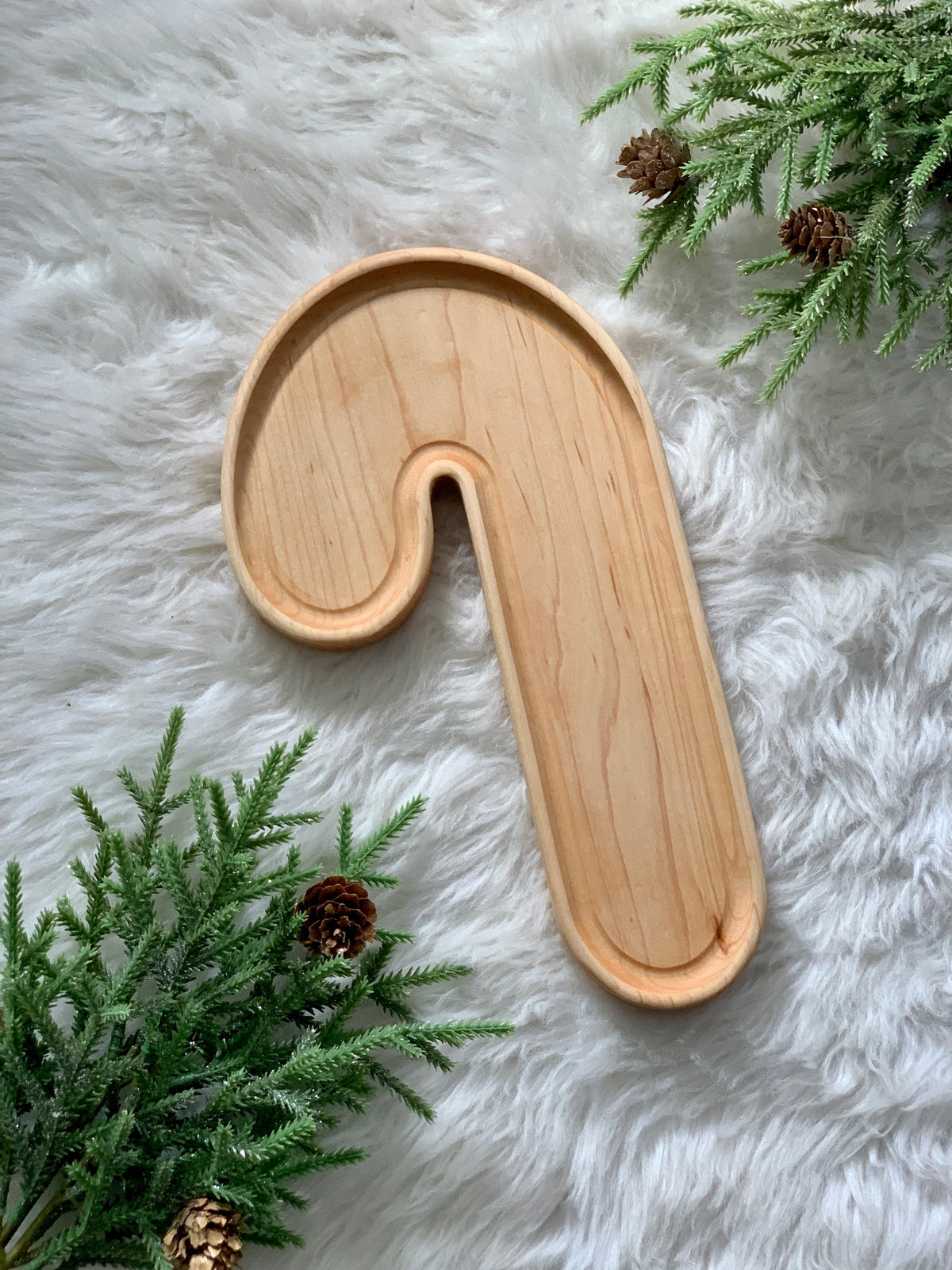 Extra large wooden candy cane-shaped sensory tray on white fur background with pine branches and pinecones