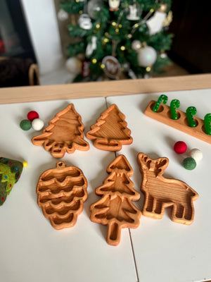 Hand-carved wooden trays shaped like pinecone, fir trees, and a reindeer arranged on white table with holiday decor