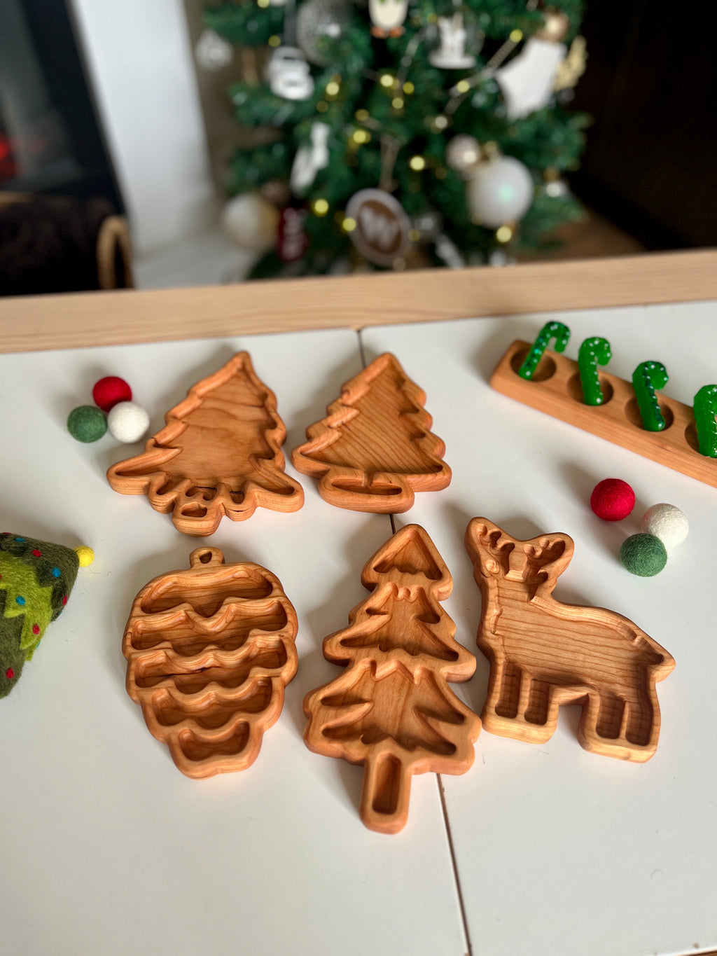 Hand-carved wooden trays shaped like pinecone, fir trees, and a reindeer arranged on white table with holiday decor