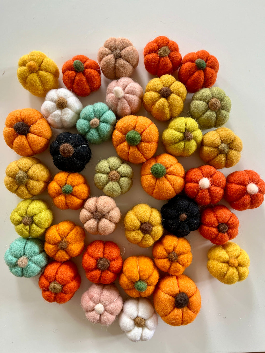 Assorted small felt pumpkins in various colors arranged in a circular pattern on a white surface