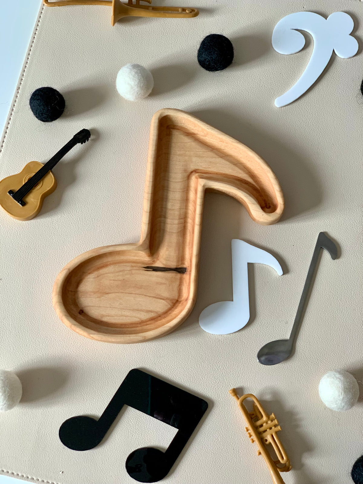 Wooden tray shaped like a music note surrounded by small felt balls, miniature instruments, and paper music symbols on light surface