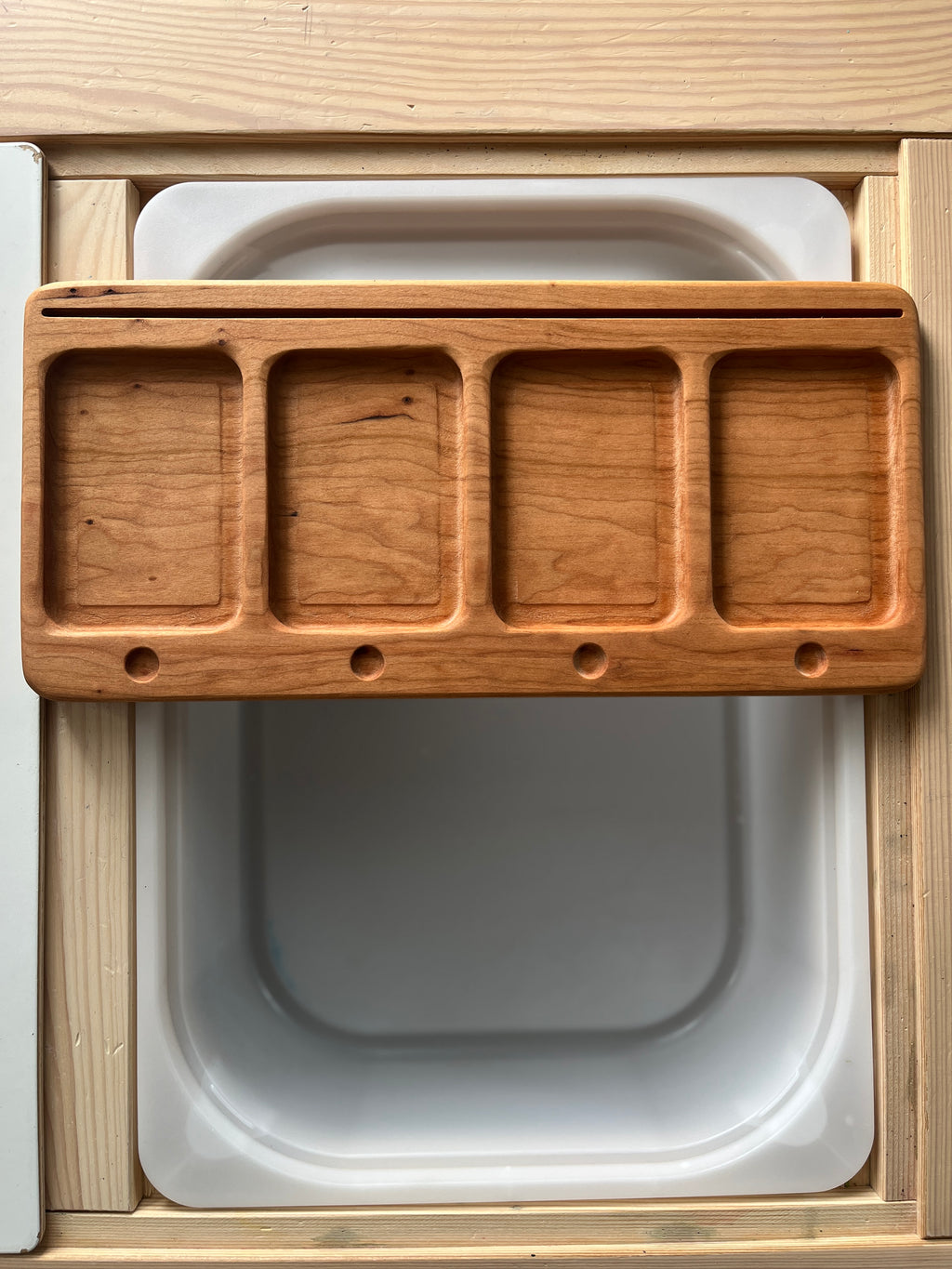 Rectangular wooden tray with four compartment slots and small holes below each slot on a light wood surface