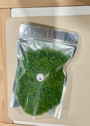 Clear resealable bag filled with finely chopped fresh green herbs on a beige surface with wooden edges