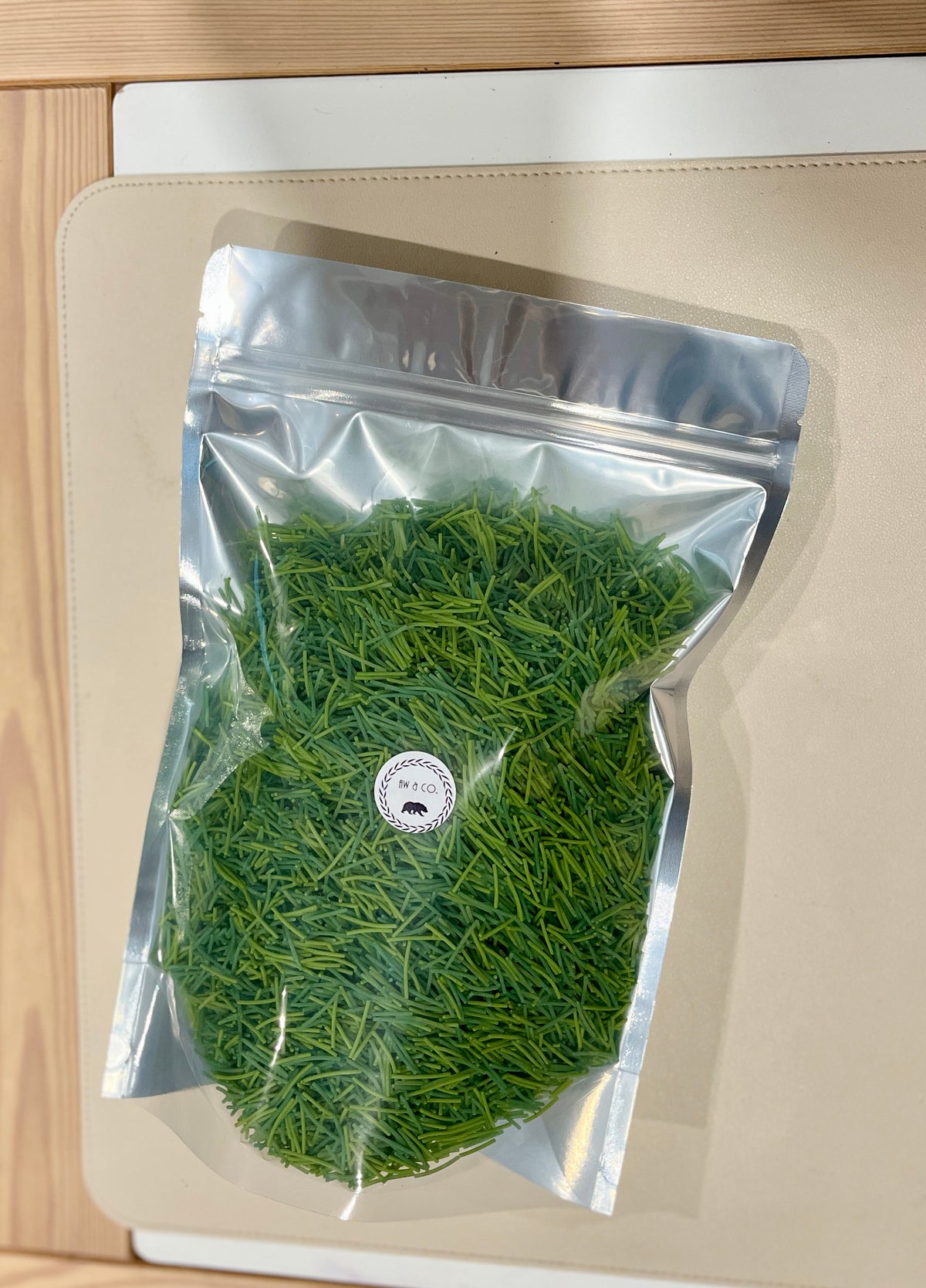 Clear resealable bag filled with finely chopped fresh green herbs on a beige surface with wooden edges