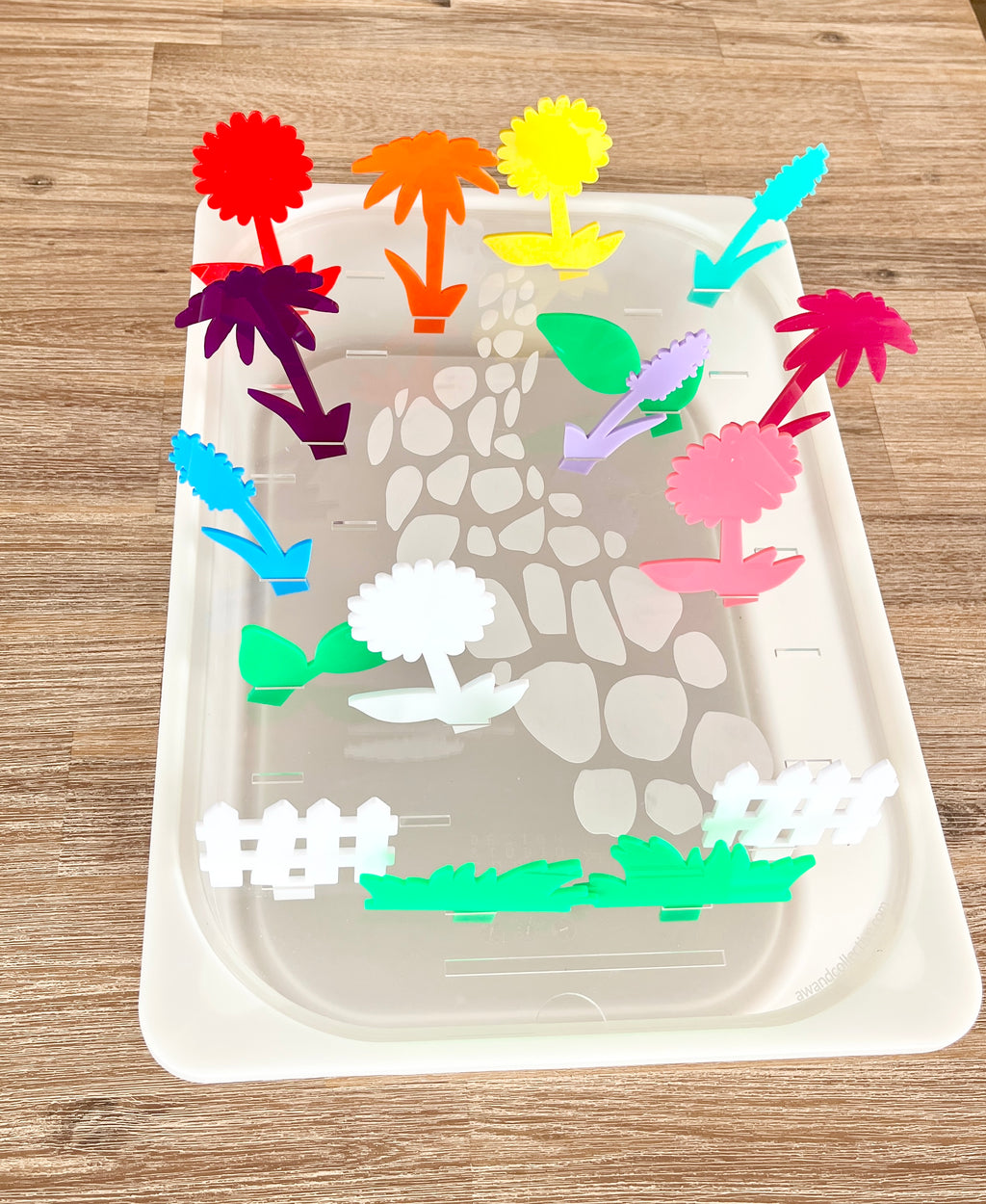 Colorful translucent acrylic pegs shaped like various plants and garden elements inserted into a white tray with a stone path design, featuring STEM Insert – Acrylic Insert with Different Peg Options - Neighborhood, Veggie Garden, Flower Garden, Under the Sea + More, handcrafted homeschool education resources.