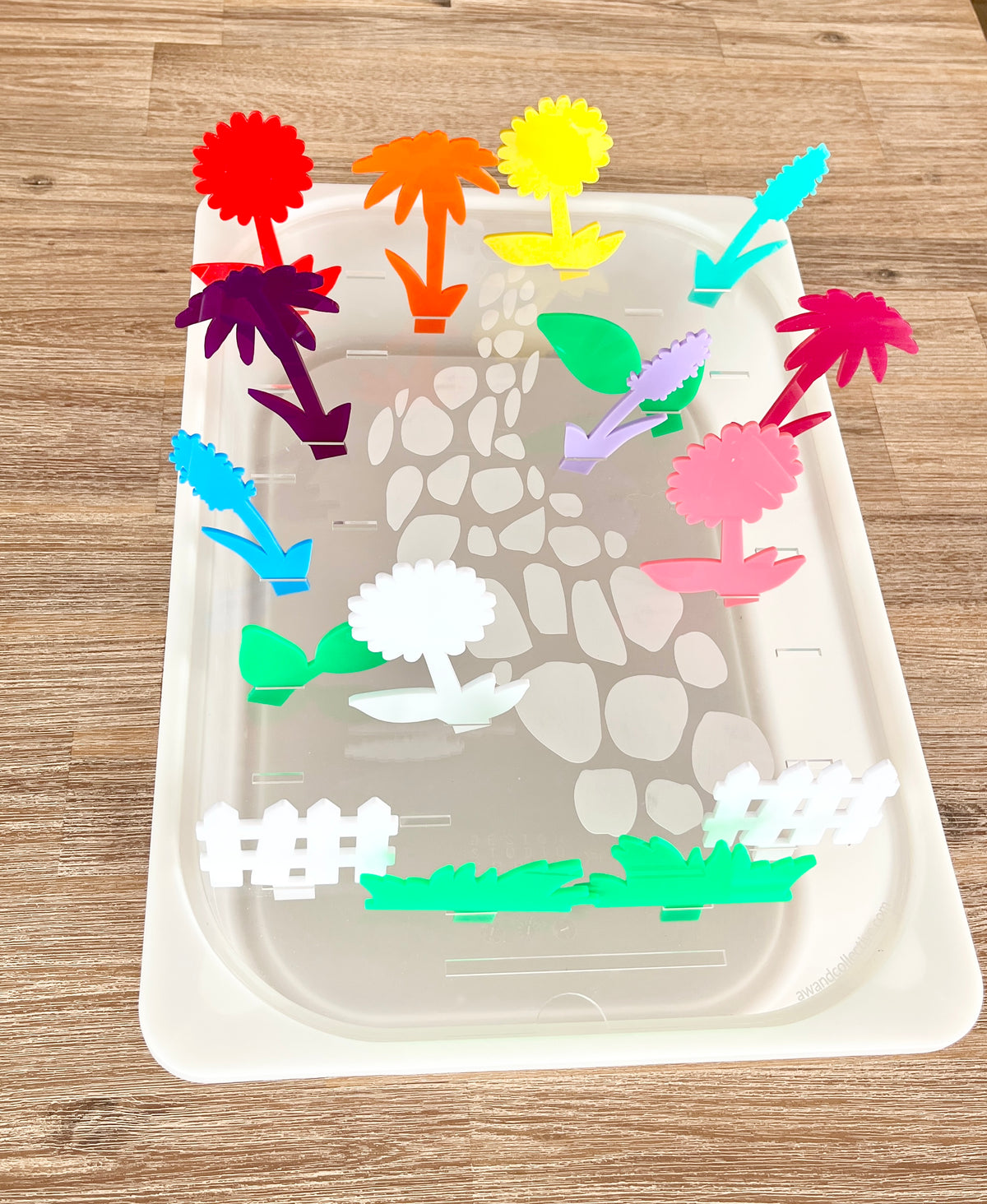 Colorful translucent acrylic pegs shaped like various plants and garden elements inserted into a white tray with a stone path design, featuring STEM Insert – Acrylic Insert with Different Peg Options - Neighborhood, Veggie Garden, Flower Garden, Under the Sea + More, handcrafted homeschool education resources.