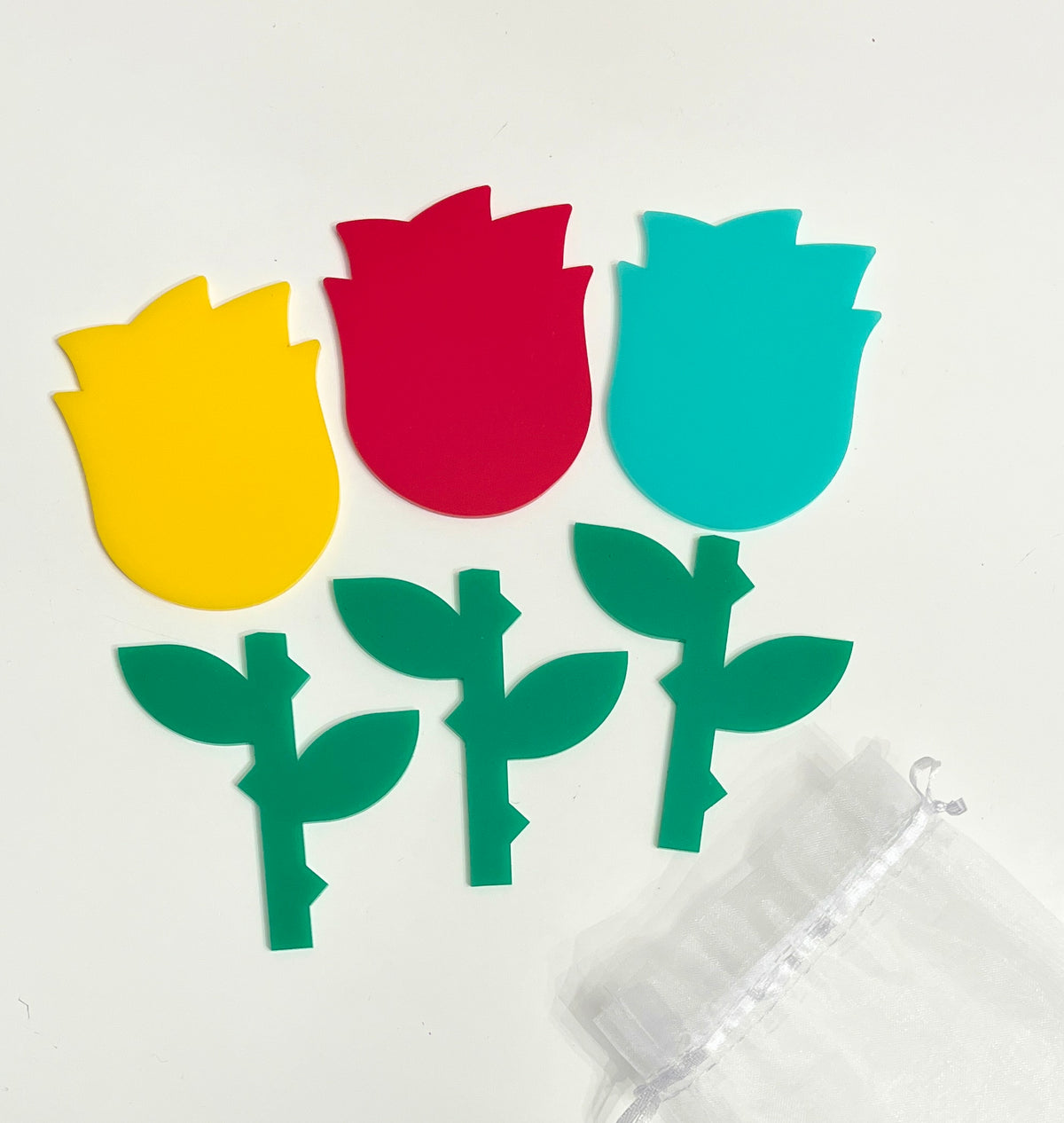 Three colorful acrylic tulip tops in yellow, red, and teal with matching green stems on white background with sheer bag