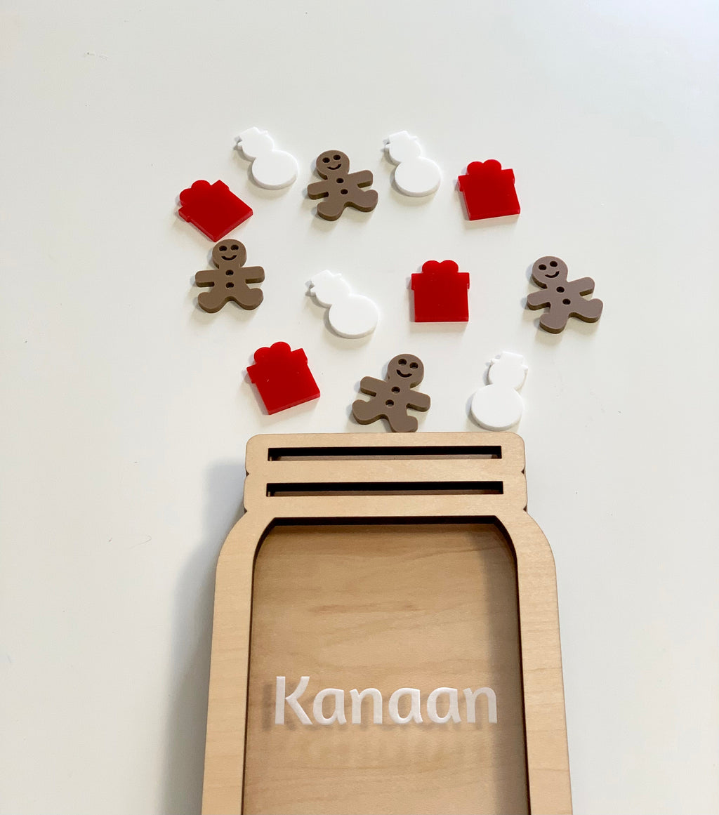Light wooden jar-shaped frame personalized with the name Kanaan and scattered red gift, white snowman, and brown gingerbread tokens above