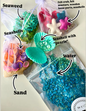 Clear bags with colorful seashells, seaweed, sand, blue ring beads, felt sea stars, crab, wooden shapes, and a plastic shell container.
