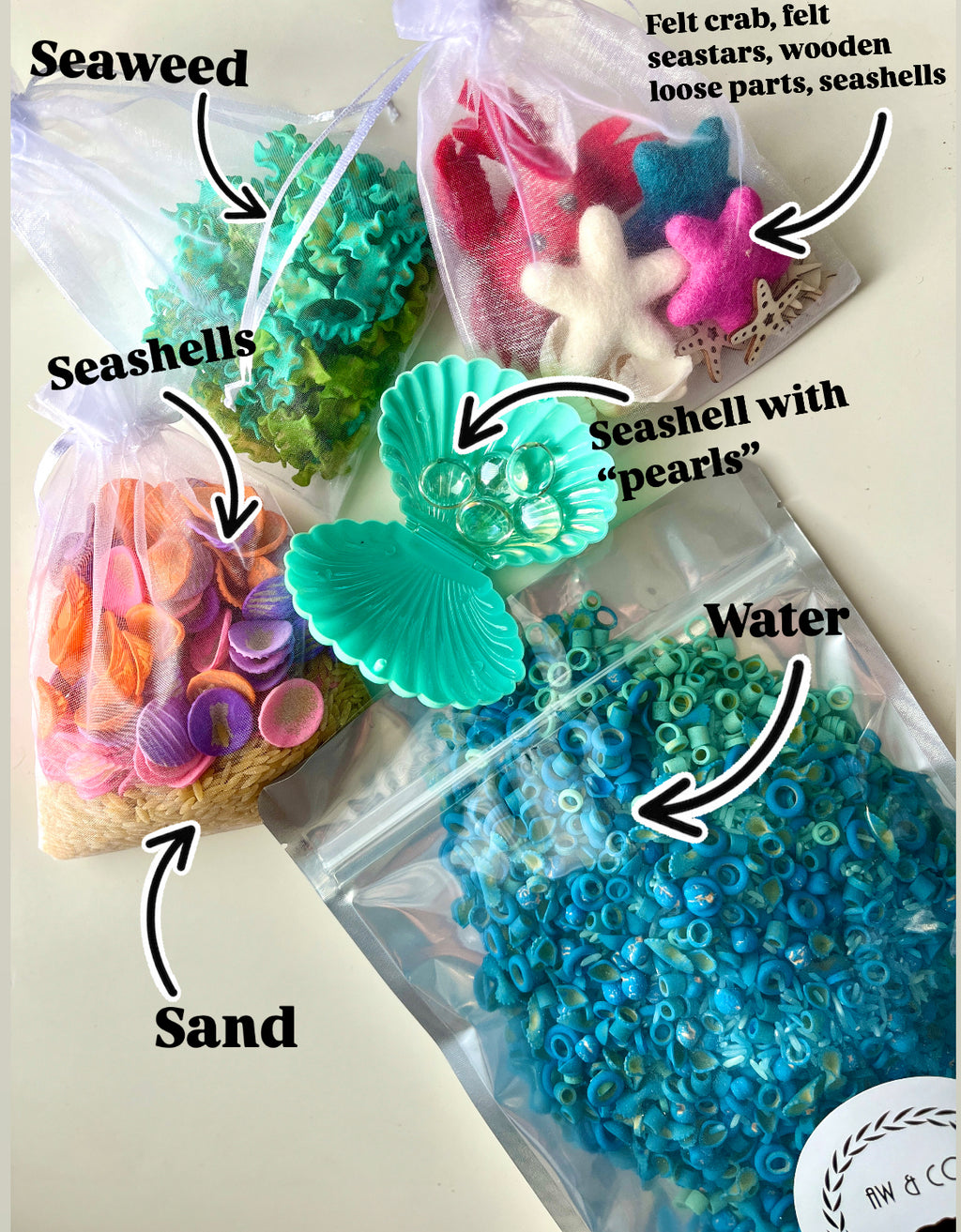 Clear bags with colorful seashells, seaweed, sand, blue ring beads, felt sea stars, crab, wooden shapes, and a plastic shell container.