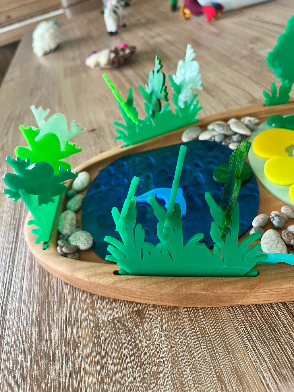 Multipurpose Oval Sensory Tray showcasing a wooden tray with blue textured pond, translucent green plant shapes, smooth natural stones, handcrafted, homeschool, education resources.