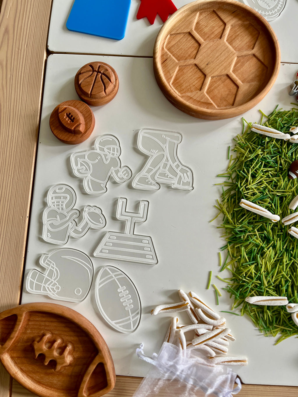 Clear plastic cookie cutters shaped like football players, helmet, goalpost, and football with wooden trays and green craft grass