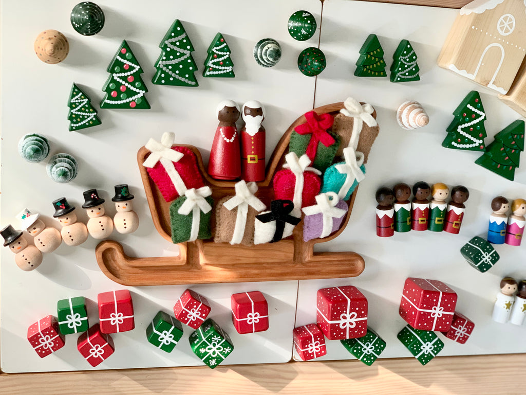 Hand-painted wooden Christmas peg dolls with Santa, Mrs Claus, snowmen, reindeer, elves, gifts, trees, and decorations on white surface
