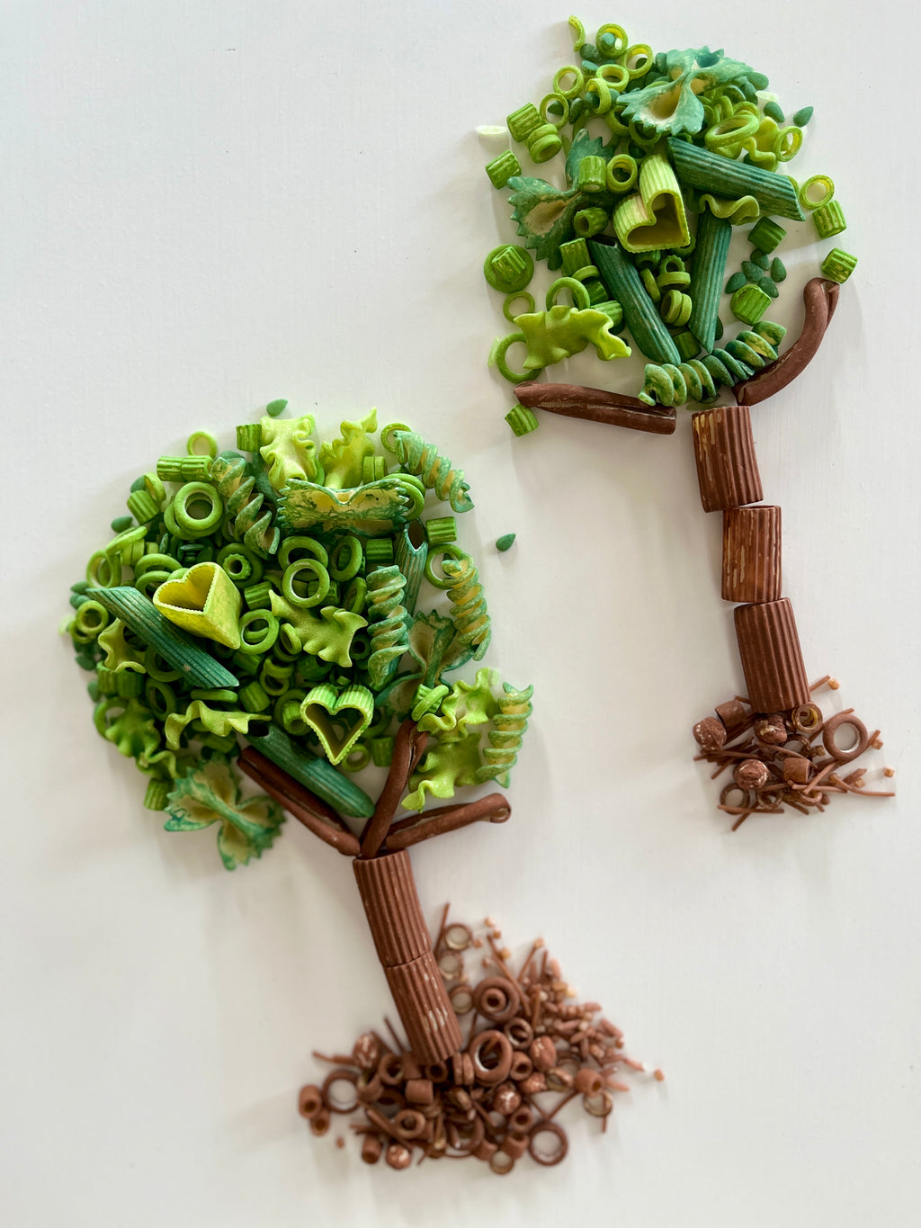 Two stylized trees crafted from various shapes and colors of green and brown pasta on a white background