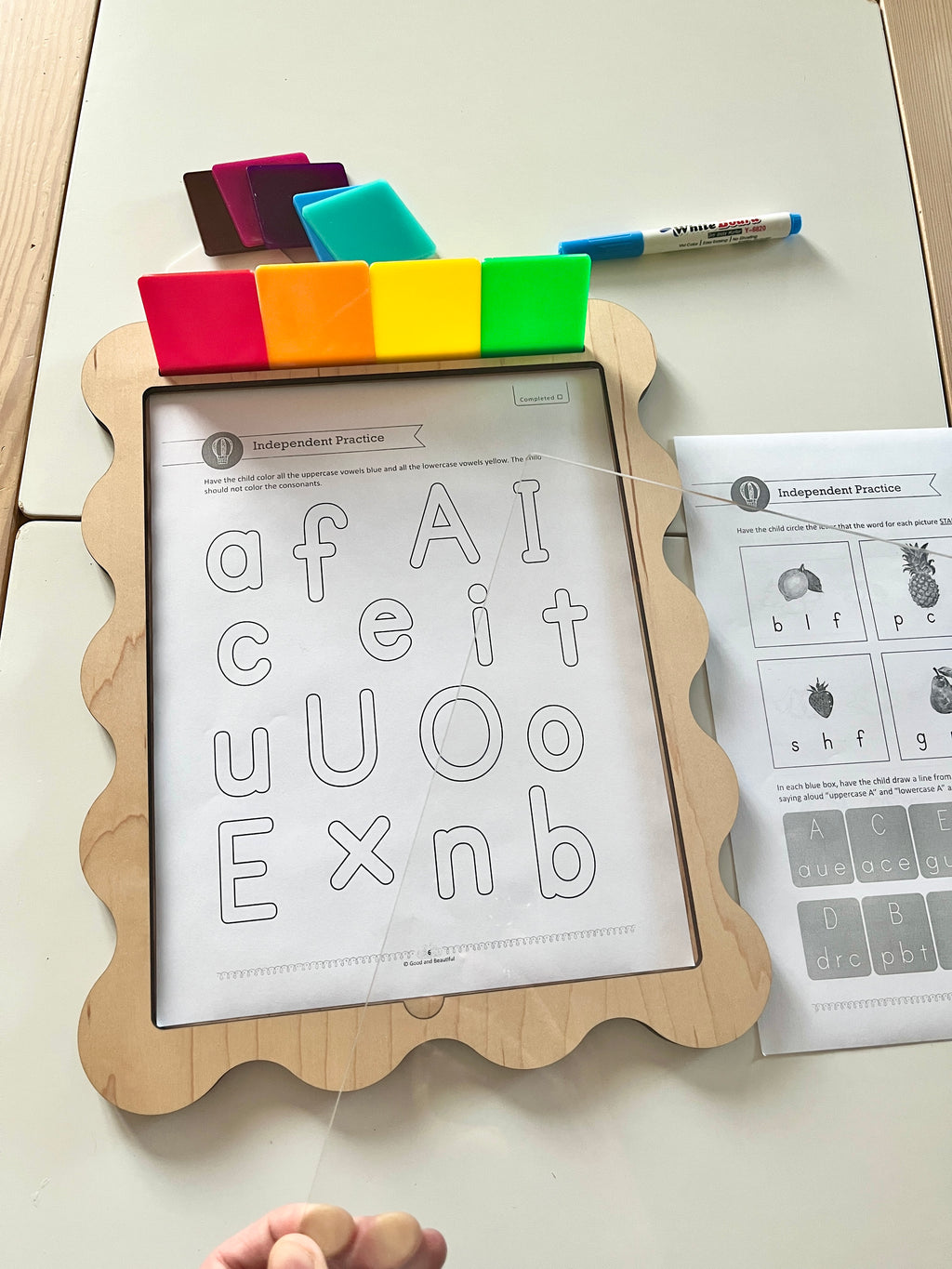 Wooden-framed activity board with scalloped edges, translucent colored tiles, alphabet worksheet, and dry erase marker on table