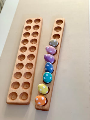 Two wooden boards with circular indentations, one holding colorful polka-dotted fabric eggs on a beige surface