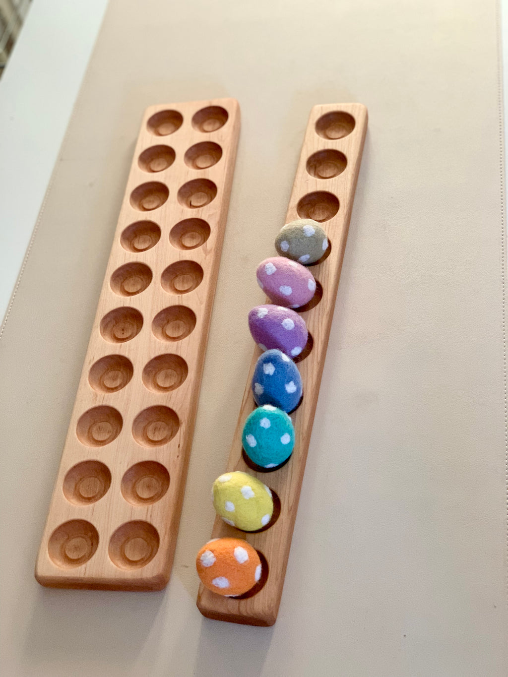 Two wooden boards with circular indentations, one holding colorful polka-dotted fabric eggs on a beige surface