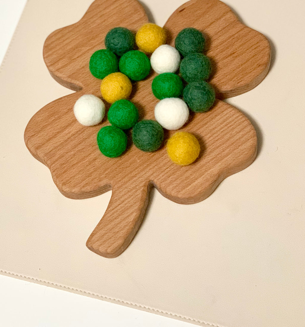 Wooden clover-shaped board topped with green, yellow, and white felt balls on a pale background