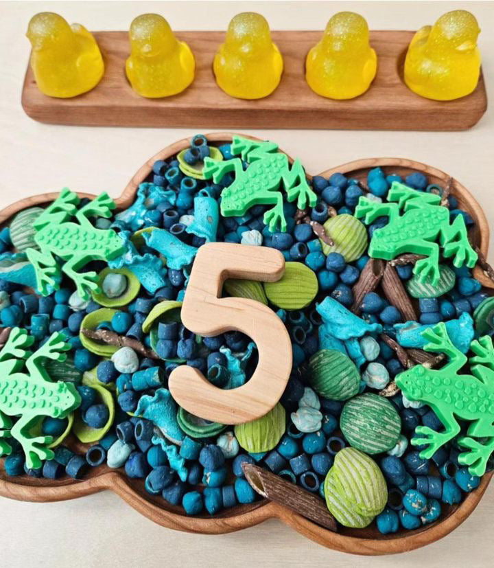 Cloud-shaped wooden sensory tray filled with blue sensory beads, green frogs, and wooden number 5 on light surface