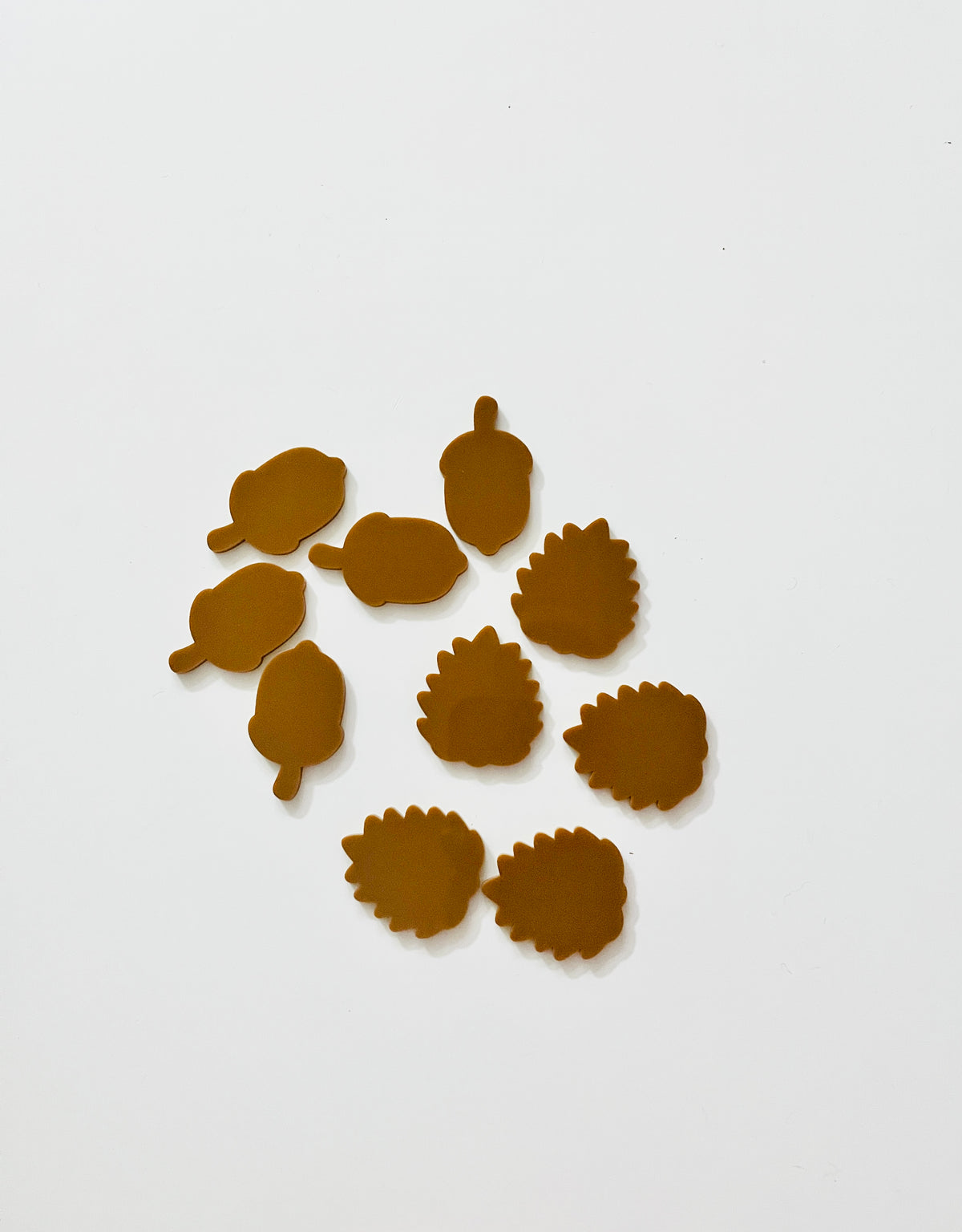 Assorted small brown felt leaves and acorns scattered on plain white background