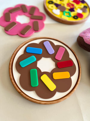 Wooden toy donut with colorful block sprinkles on a light surface near other toy pastries and donuts