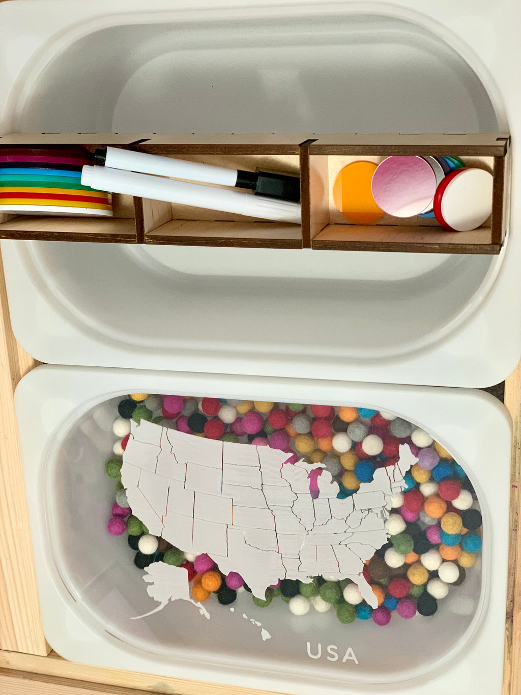 White plastic container lid with a puzzle of the USA map on colorful felt balls and a wooden divider holding markers and tokens above it