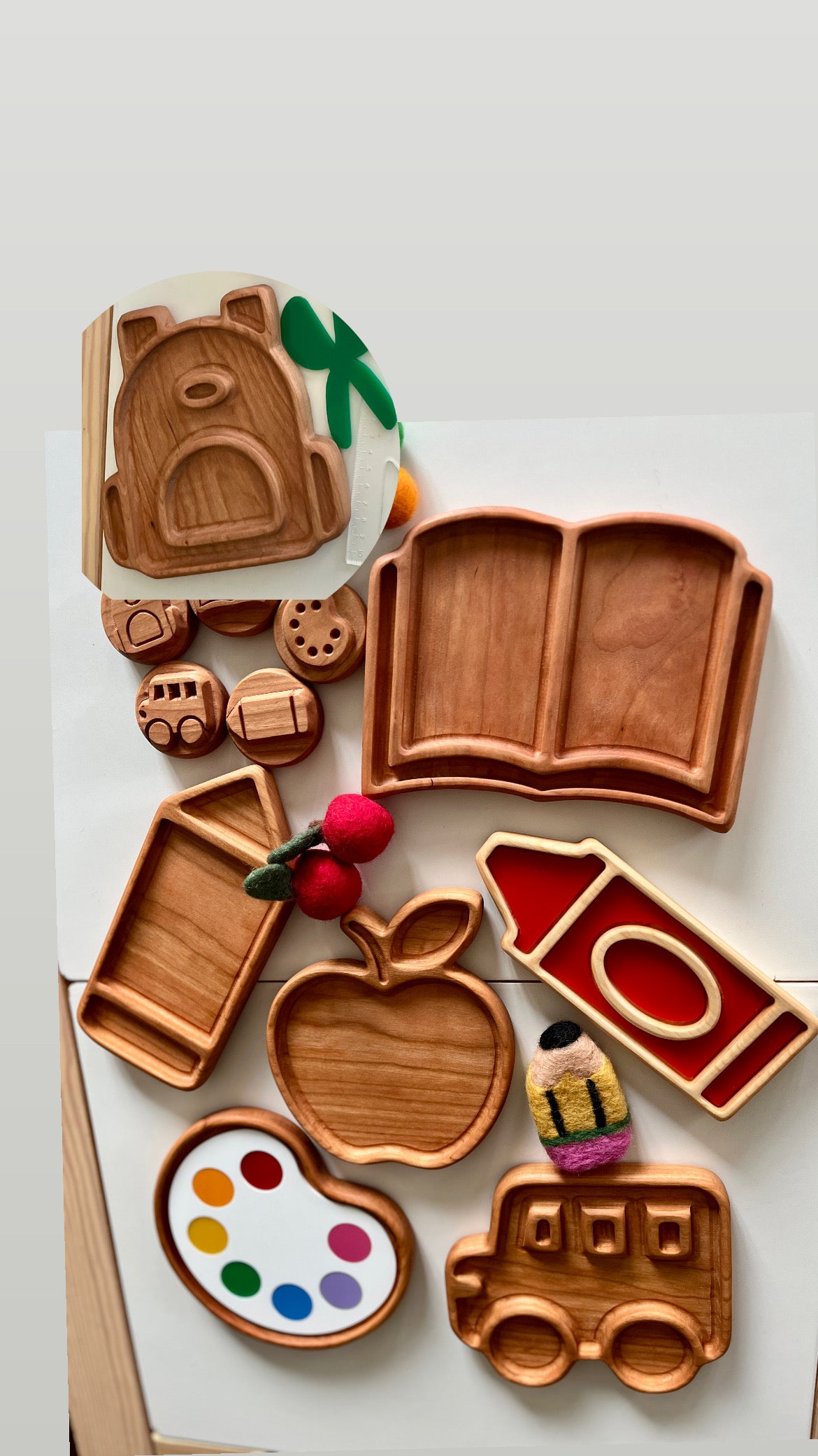 Wooden trays shaped like book, pencil, apple, bus, paint palette, and schoolhouse with matching wooden tokens on white surface